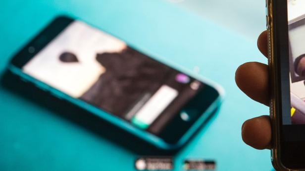 Eine Person hält ein Smartphone in der Hand, während ein anderes Smartphone auf einem türkisfarbenen Hintergrund liegt.