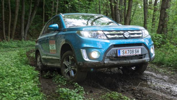 Ein blauer Suzuki fährt auf einer schlammigen Waldstraße.