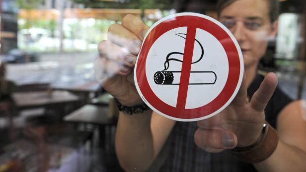 Eine Person hält ein „Rauchen verboten“-Schild vor einem Fenster.