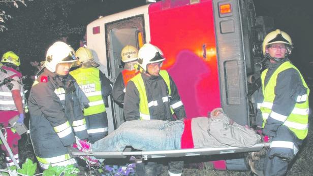 Feuerwehrleute tragen eine verletzte Person auf einer Trage zu einem Krankenwagen.