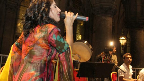 Eine Sängerin tritt mit einem Mikrofon vor einer Band auf einer Bühne auf.