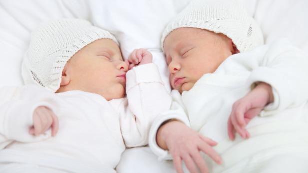 Zwei schlafende Babys liegen nebeneinander in weißen Mützen.