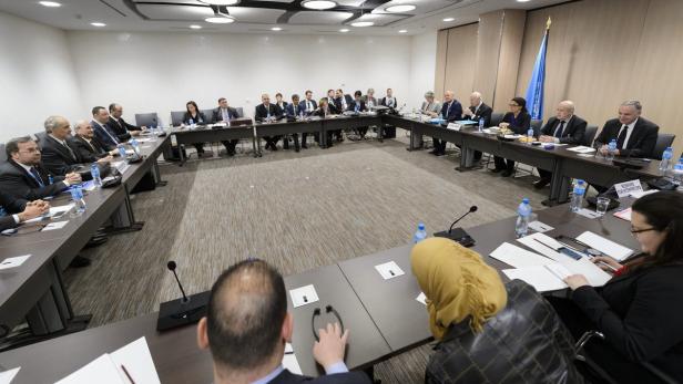 Eine Gruppe von Menschen sitzt an einem U-förmigen Tisch in einem Konferenzraum.