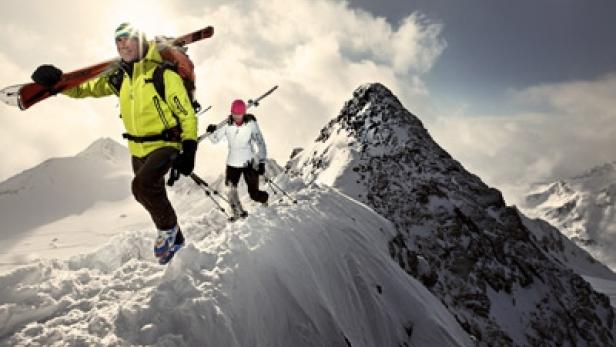 Zwei Skibergsteiger steigen mit Skiern auf den Gipfel eines schneebedeckten Berges.