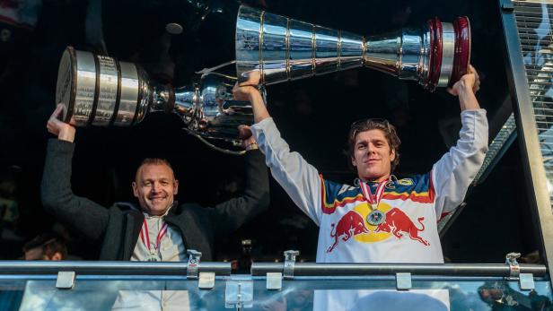 Zwei Männer halten Trophäen in die Höhe, der eine trägt ein Red Bull-Trikot und eine Medaille.