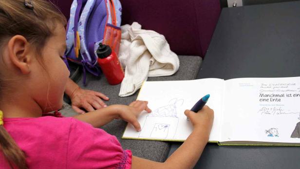 Ein Mädchen zeichnet mit einem blauen Stift ein Haus in ein Buch.