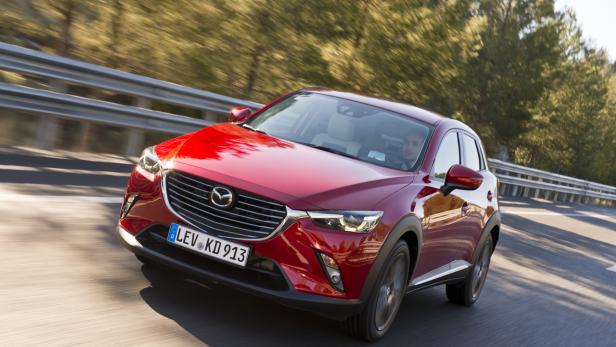 Ein roter Mazda CX-3 fährt auf einer Landstraße.