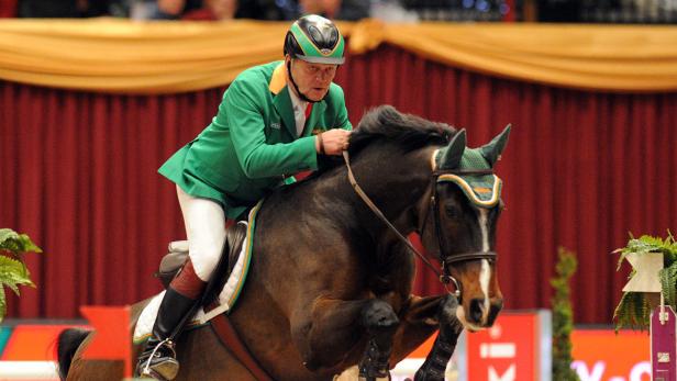 Ein Reiter in grüner Jacke auf einem braunen Pferd bei einem Reitturnier.