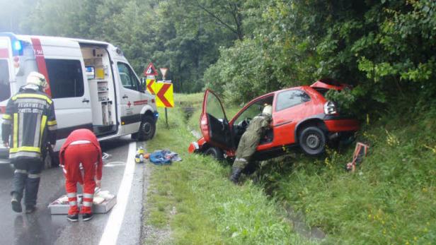Ein rotes Auto ist nach einem Unfall in einem Graben gelandet; Rettungskräfte sind vor Ort.