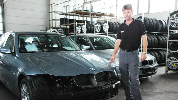 Ein Mann steht in einer Werkstatt vor zwei BMWs und einem Reifenregal.