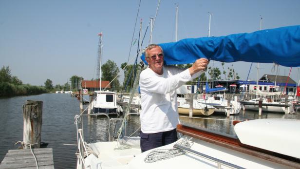 Ein Mann befestigt eine blaue Persenning an einem Segelboot in einem Hafen.