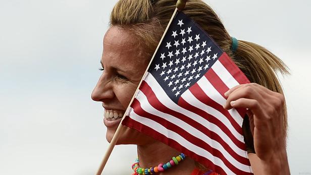 Eine Frau hält eine amerikanische Flagge hoch und lächelt.