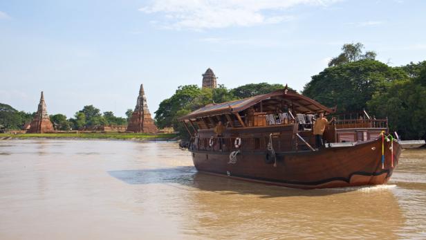Langsam gleitet die Mekhala, eine zum Hotelschiff adaptierte Reisbarke, über den Chao Phraya. An den Ufern des Stromes ziehen Tempel und goldglänzende Buddhas vorbei, auch einfache Hütten auf Holzstelzen, schmucke Villen und großflächige Teppiche aus Wasserhyazinthen.
