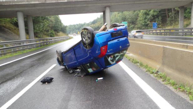 Ein blaues Auto liegt nach einem Unfall auf einer Autobahn auf dem Dach.