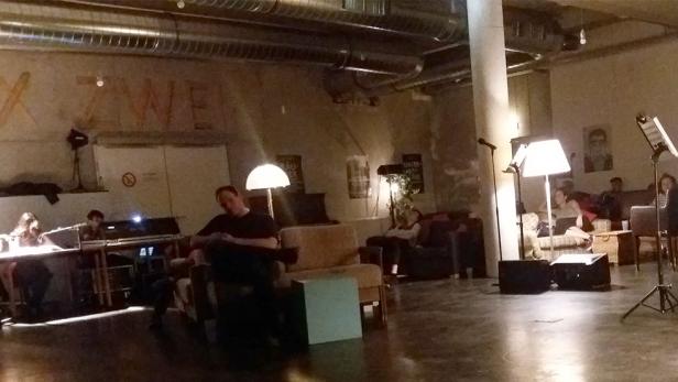 In einem Raum mit Bühne und Publikum liest ein Mann an einem Mikrofon.