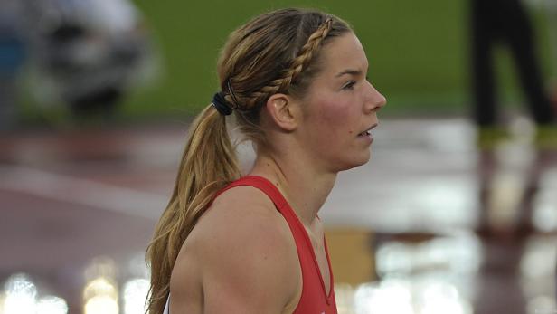 Eine blonde Frau mit Zöpfen und einem roten Sporttop auf einer Laufbahn.