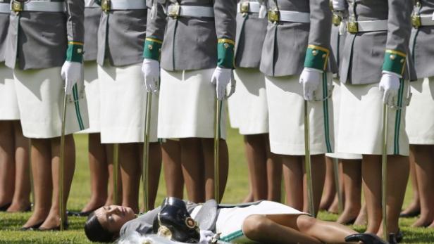 Eine Kadettin liegt ohnmächtig auf dem Rasen, während andere in Formation stehen.