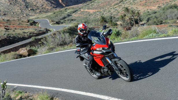 Ein Motorradfahrer fährt auf einer roten Ducati eine kurvenreiche Straße entlang.