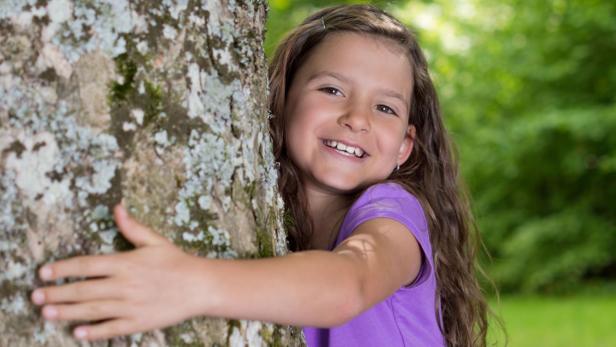 Ein lächelndes Mädchen umarmt einen Baum im Wald.