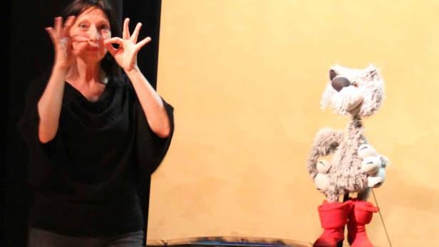 Eine Frau führt ein Puppenspiel mit einer Wolfspuppe in roten Stiefeln auf.