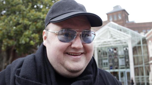Ein lächelnder Mann mit Sonnenbrille und Mütze vor einem Gebäude.