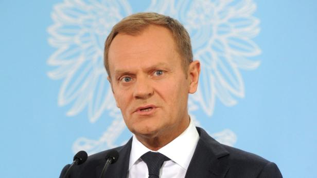 Donald Tusk spricht vor einem hellblauen Hintergrund mit einem stilisierten Adler.