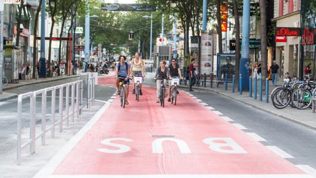 Eine Gruppe von Radfahrern fährt auf einer rot markierten Busspur in einer Stadt.