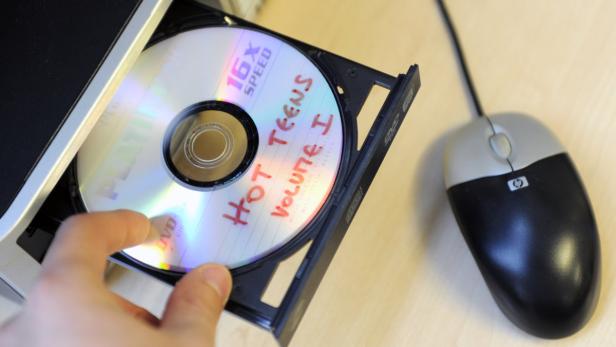 Eine Hand legt eine DVD mit der Aufschrift „Hot Teens Volume I“ in ein Laufwerk.