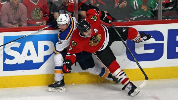 Zwei Eishockeyspieler kämpfen um den Puck an der Bande.