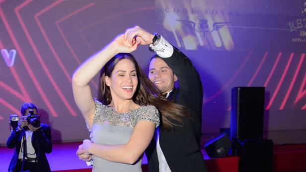 Ein Paar tanzt lächelnd auf einer Veranstaltung vor einer Bühne.