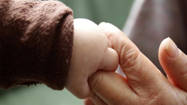 Die Hand eines Babys umklammert den Finger eines Erwachsenen.