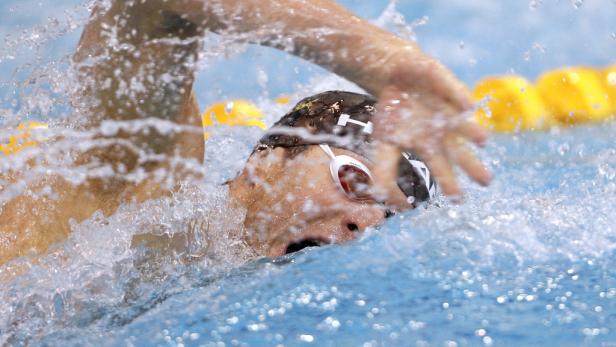 Ein Schwimmer im Wettkampf, umgeben von Spritzwasser.