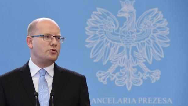 Ein Mann mit Brille spricht vor dem Hintergrund des polnischen Wappens.