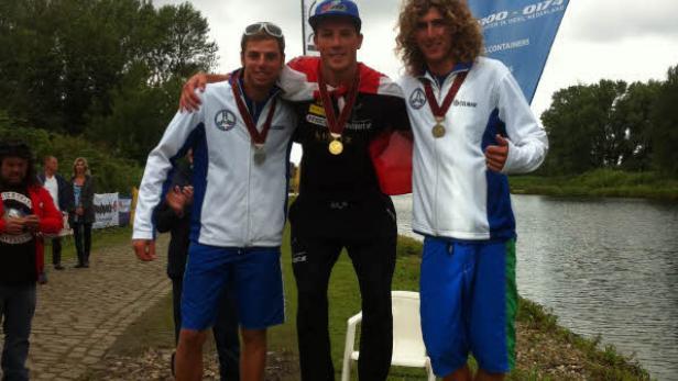 Drei Männer stehen mit Medaillen auf einem Siegerpodest aus Holzwürfeln.