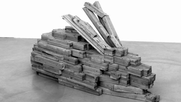 Eine Skulptur aus gestapelten Holzblöcken und Balken in einem Innenraum.