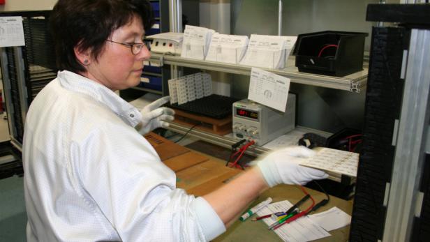 Eine Frau arbeitet mit Handschuhen an elektronischen Bauteilen in einer Werkstatt.