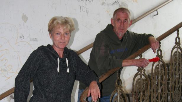 Ein Mann und eine Frau stehen an einem Treppengeländer in einem Haus mit beschmierten Wänden.