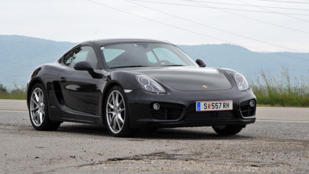 Ein schwarzer Porsche Cayman steht auf einer asphaltierten Straße.
