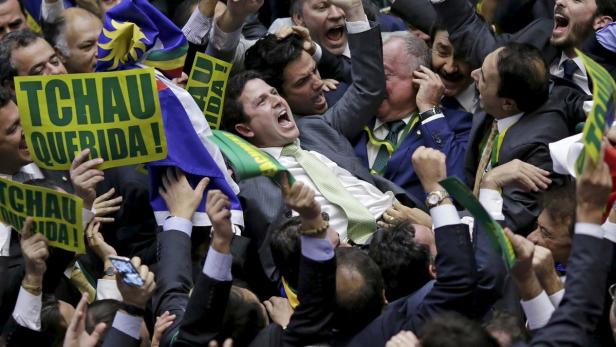 Menschen jubeln und halten Schilder mit der Aufschrift „Tchau Querida!“ hoch.