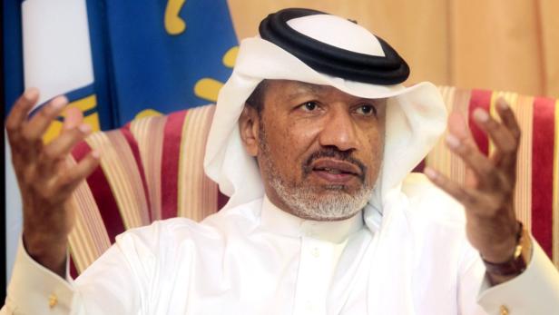 Ein Mann mit traditioneller Kopfbedeckung gestikuliert vor einer Flagge.