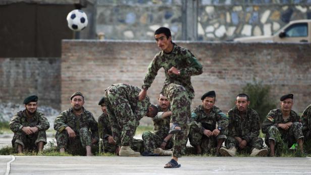 Eine Gruppe Soldaten in Tarnuniform spielt mit einem Fußball.