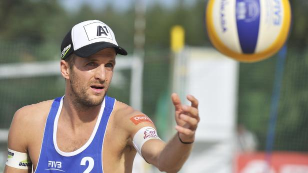 Ein Beachvolleyballspieler mit Kappe bereitet sich auf einen Aufschlag vor.