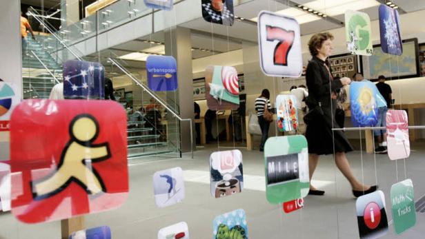 In einem Apple Store hängen App-Logos von der Decke, während eine Frau vorbeigeht.