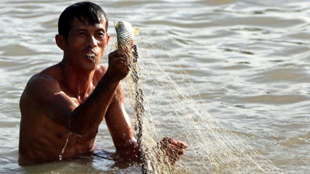 Ein Fischer steht im Wasser und hält ein Netz mit einem Fisch darin.