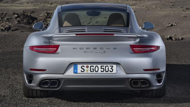 Die Rückansicht eines silbernen Porsche 911 Turbo S auf einer Schotterfläche.
