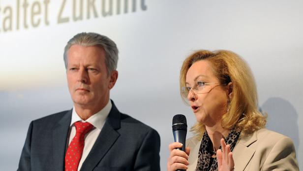 Eine Frau spricht bei einer Veranstaltung in ein Mikrofon, neben ihr steht ein Mann im Anzug.