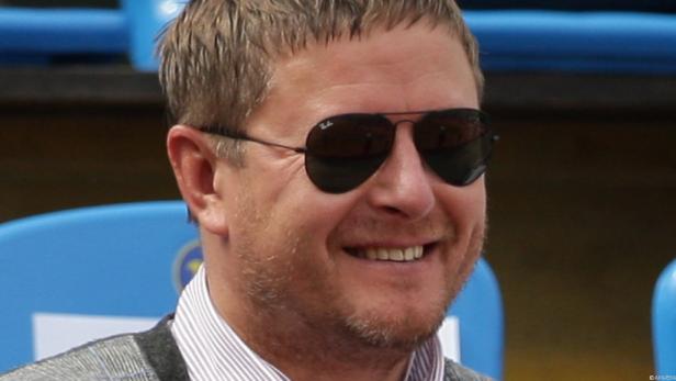 Ein lächelnder Mann mit Sonnenbrille und grau melierter Jacke.