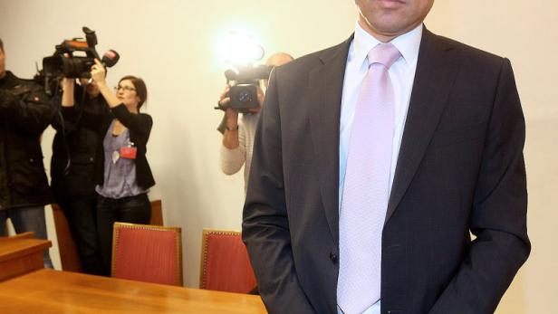 Ein Mann im Anzug steht vor einer Gruppe von Reportern und Kameras.