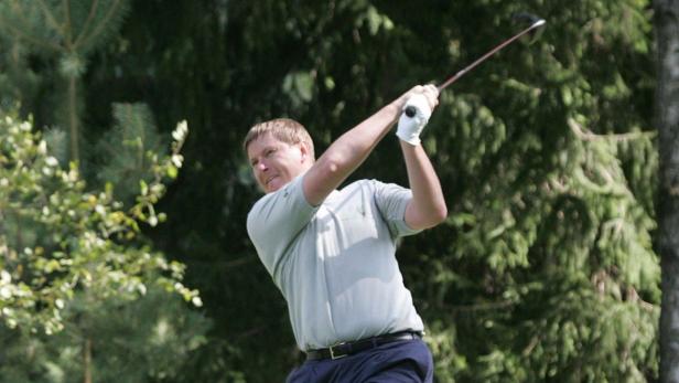 Ein Mann schwingt einen Golfschläger vor einem Hintergrund aus Bäumen.