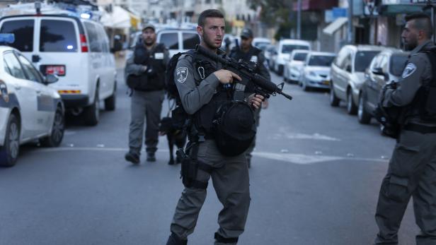 Ein bewaffneter Polizist steht auf einer Straße mit Autos und anderen Polizisten.